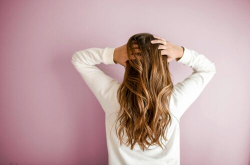 Back view of a woman with elegant long brown hair against a pink wall, showcasing stylish hair design.